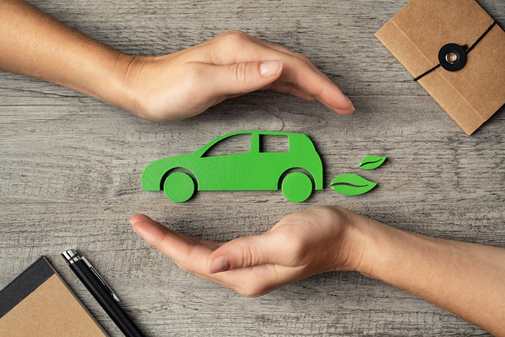 Close up of hands of woman protecting icon of green eco-friendly car over wooden table